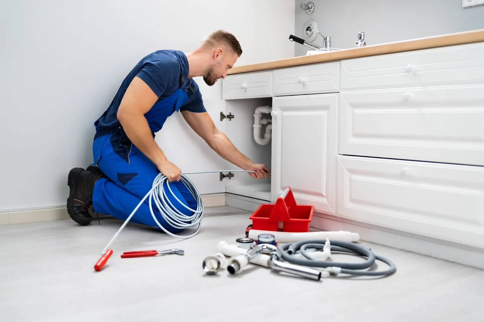 A man in blue overalls repairs a sink, addressing plumbing issues to prevent clogged drains effectively.