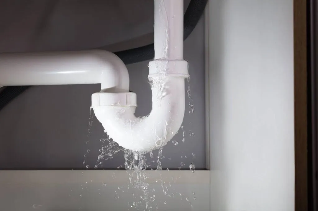 A white pipe mounted on a wall is leaking water, creating a small drip below it