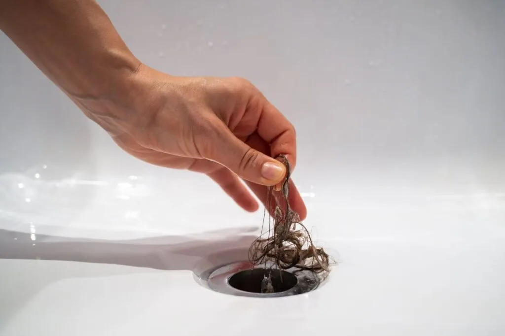 A hand grips hair above a sink, capturing hair maintenance