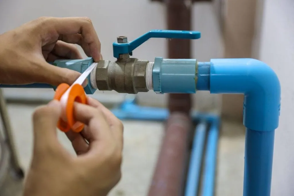A person repairs a pipe adjusting a blue valve with tools in hand