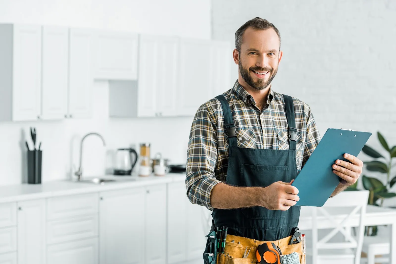 Plumber with a clipboard standing in a modern kitchen.