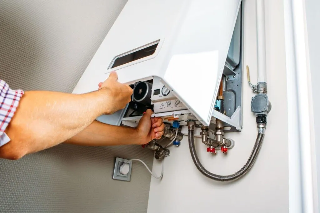 A man repairs a gas boiler in a utility room focused on the equipment and surrounded by tools and parts